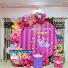 A playful Peppa Pig theme for Ishani's 2nd birthday. The setup includes a striped pink backdrop with Peppa, a colorful balloon arch, and a themed cake stand.