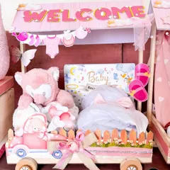 A close-up of one of the carriages from the 'Welcome Baby' train, filled with a soft teddy bear, baby record book, and other adorable pink-themed gifts.