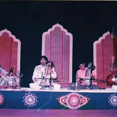 A photograph from an older concert, performing with a full Indian classical ensemble. I am providing the rhythmic foundation for sarangi, esraj, and tanpura players on a traditionally decorated stage.