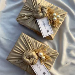A close-up of my signature satin fabric wrap. This elegant gold wrapping, complete with a 'Best Wishes' tag and pearl accents, elevates any gift.