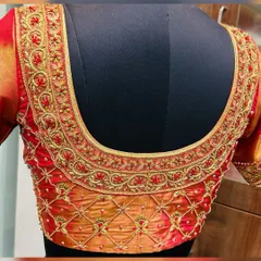 For the classic bride, this dual-tone red and orange silk blouse is a timeless choice. The U-shaped back is adorned with traditional floral vine aari work in gold thread, creating an opulent look that perfectly complements a wedding saree.