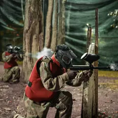 Aim, shoot, conquer. A player takes cover and returns fire in our paintball arena. We provide full camouflage gear and masks for an immersive experience.