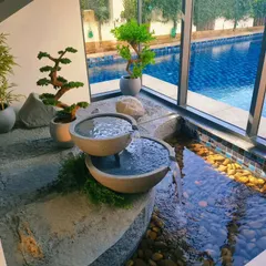 This bespoke indoor water feature transforms an underutilized corner into a tranquil zen garden. The gentle sound of water, combined with curated bonsai and bamboo, creates a peaceful focal point that connects the home's interior with the poolside view.