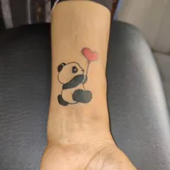 A cute and simple panda tattoo on the wrist, holding a red heart-shaped balloon. This shows that minimalist tattoos can also be playful and colorful.