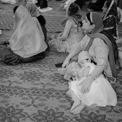 A touching black and white photo of a young child asleep in her mother's lap during a ceremony. This quiet, candid moment beautifully illustrates the peaceful trust between a mother and child.