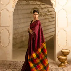 An editorial-style photograph for Kumaran Silks, showcasing a traditional saree in a grand, architectural setting. The lighting and composition are designed to highlight the fabric's drape, rich color, and the intricate pattern of the pallu, creating an aspirational look for fashion brands.