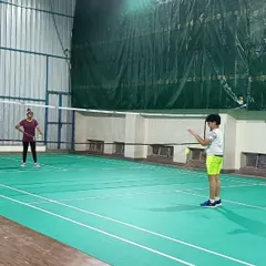 A young player prepares to serve while his partner stands ready. This image captures a moment of focus during a kids' badminton coaching session.