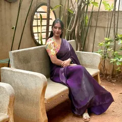 A candid moment, sitting on a bench in a garden. The soft fabric of the purple saree drapes so beautifully, making it feel both elegant and comfortable for a day out.