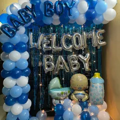 A classic welcome home decoration for a baby boy. The setup features a full balloon arch in shades of blue and white against a foil curtain, with "Welcome Baby" and "Baby Boy" foil balloons.