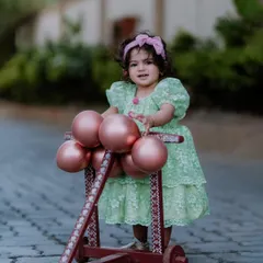 One whole year of cuteness. This full-length shot from an outdoor first birthday photoshoot captures the little one standing confidently with her walker, dressed in a beautiful lacy green dress.
