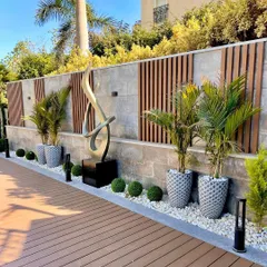 A beautiful example of landscape design featuring a wooden deck, modern planters with palm trees, and a striking abstract sculpture, all working together to create a harmonious environment.