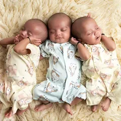 A more candid shot of the triplets in matching onesies, stretching and sleeping together. These natural moments are just as precious.