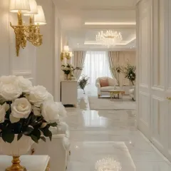 This hallway connects the living spaces in a luxury home, designed with white marble floors and intricate wall paneling. The classic wall lamps and a view into the plush living area demonstrate my approach to creating a consistent and elegant design story throughout the entire home.