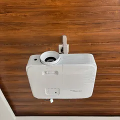 A close up of a ceiling mounted Optoma HD projector against a wooden ceiling. This shows how we can adapt the installation to different ceiling materials and styles for a secure and seamless fit.