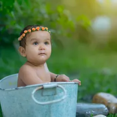 An outdoor bath time-themed portrait. The natural light and green surroundings add a fresh, sweet feel to this baby's photoshoot in a rustic metal tub.
