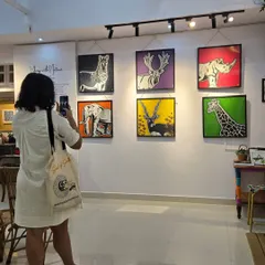 A visitor captures a photo of the vibrant, pop-art-style wildlife paintings from the "Vibing with Nature" exhibition, showcasing endangered animals in bold colors.