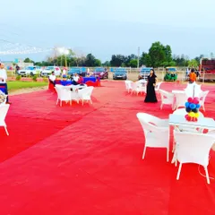 We cover large outdoor areas with carpeting to create a clean and defined party space. Here, a red carpet covers the lawn, with white garden chairs and tables set up for guests.