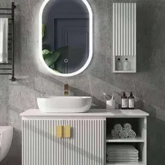 A sleek and modern bathroom design featuring a white floating vanity with reeded texture and gold hardware. The large, pill-shaped LED mirror provides excellent, soft lighting, while the open shelves offer space for neatly folded towels.