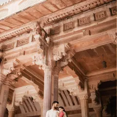 A low-angle shot looking up at a couple standing in a beautifully carved stone hall, emphasizing the intricate architecture of the Jaipur palace.