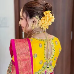 A side profile showcasing an elegant bridal updo, decorated with a large, vibrant yellow flower to match the bride's Nauvari saree.