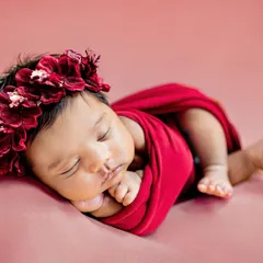 This little one looks like a beautiful rose, wrapped in red with a delicate floral crown. I use a variety of colorful wraps and props to style your newborn session.