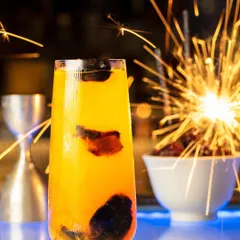 A festive cocktail shot for Hakkasan Mumbai, with a sparkler creating a celebratory feel. The bright sparks contrast beautifully with the dark background, highlighting the vibrant yellow drink.