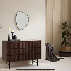 A three-drawer chest from the collection, styled in a modern room with an organic-shaped mirror and minimal decor. This shows the piece in a realistic, aspirational interior.