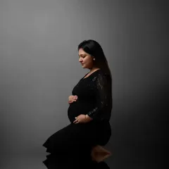This kneeling pose, combined with a reflective floor and simple grey background, creates a powerful and introspective portrait focused entirely on the mother-to-be.
