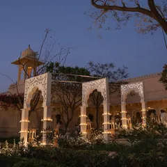 A view of the 'Sheesh Mahal' themed bar at dusk, where intricate white arches and candlelight create a regal atmosphere at The Oberoi Udaivilas.