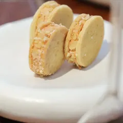 A close-up of almond sandwich cookies on a uniquely shaped white plate. This highlights the beautiful, custom tableware we often use to complement our food.