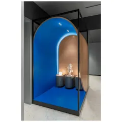 The family temple in 'A Hint of Azul' is conceptualized as a sculptural object framed within a metal wireframe. The vibrant blue interior and curved form create a distinct, holy space that can be glimpsed from the dining area.