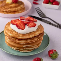 A classic breakfast or dessert: a stack of fluffy pancakes topped with fresh strawberries and cream. The clean, bright styling gives this shot a fresh and wholesome feel.