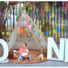 A beautiful outdoor first birthday setup with a boho-chic teepee and large 'ONE' letters. We create stunning milestone portraits in natural settings.