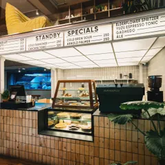 The counter is the operational heart of Stand By Coffee. This shot captures the menu board, pastry display, and high-end coffee machine, giving customers a clear view of the offerings in a setting that feels modern and welcoming.