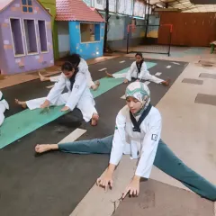 Students hold a deep stretch, working on their splits. This level of flexibility is essential for executing high kicks and advanced techniques.