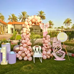 A lovely butterfly-themed first birthday in a garden. This outdoor setup features a pastel pink and rose gold balloon arch, a large butterfly cutout, and a marquee number '1', all arranged on the grass for a beautiful daytime party.