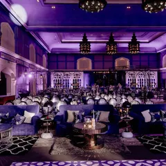 A wide view of the Sangeet hall, showing the cohesive design of the lounge seating, stage, and architectural elements. The deep blue and purple lighting scheme tied everything together for a moody, glamorous feel.