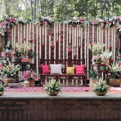A beautiful rustic Mehendi stage setup against a brick wall. We used hanging strings of tuberose, lush floral arrangements in brass pots, and traditional wooden seating to create a warm and earthy vibe.