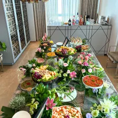 A fresh and vibrant grazing table perfect for a daytime event or brunch. This beautiful spread is filled with colorful salads, light bites, and fresh pizzas, surrounded by lush floral arrangements on a modern marble tabletop.