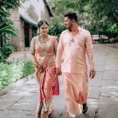 A candid moment between a couple, both dressed in our custom designs. She wears a stunning peach and silver Kanchipuram silk saree, while he complements her in a matching peach silk shirt and traditional panche.