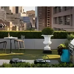 A rooftop patio designed for entertaining, featuring an outdoor kitchenette and bar-height seating with a stunning city view. The use of artificial turf and manicured hedges creates a lush, garden-like feel in an urban setting.
