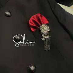 A detailed shot of a pocket on a black Jodhpuri jacket, adorned with a red silk pocket square and a custom silver brooch. Accessories are key to completing the look.