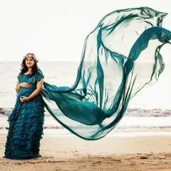 A beachside maternity shoot is the perfect setting for this flowing teal gown. The dress features a long trail that catches the ocean breeze, adding beautiful movement and a touch of drama to your photos.