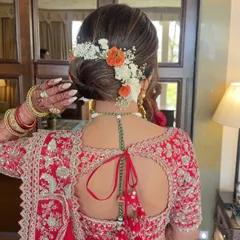 For this beautiful bride in a red lehenga, I crafted a clean, low bridal bun and decorated it with a combination of white and orange fresh flowers. This style is perfect for keeping the focus on the bride's outfit and jewelry while adding a touch of natural beauty.