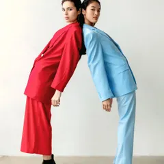 The models stand back-to-back, leaning on each other, their contrasting suits creating a visually striking composition that plays with color and form.