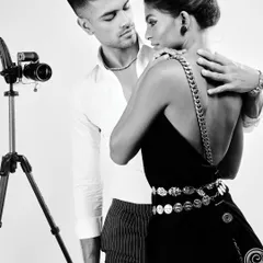 Part of the same editorial, this image expands the scene to include a vintage camera prop. The black and white treatment adds a timeless, classic feel to this romantic couple's portrait, where the coin belt and chain strap add textural details.