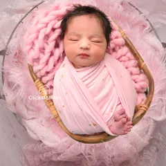 Pretty in pink. This baby girl is nestled in a basket with soft pink blankets, swaddled in a wrap with tiny gold stars.