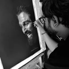 A black and white photo of me at work on the Allu Arjun portrait. This behind-the-scenes shot shows the process of building up layers of charcoal to achieve a realistic likeness.
