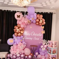 A beautiful butterfly-themed baby shower decoration. This setup uses a soft palette of pink, purple, and rose gold balloons, a personalized "Baby Chawla Coming Soon" backdrop, and charming details like butterfly accents and 'BABY' blocks.