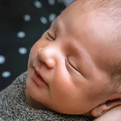 A close-up of a newborn's face, showing their peaceful sleep. The focus is entirely on the baby, with no distracting props.